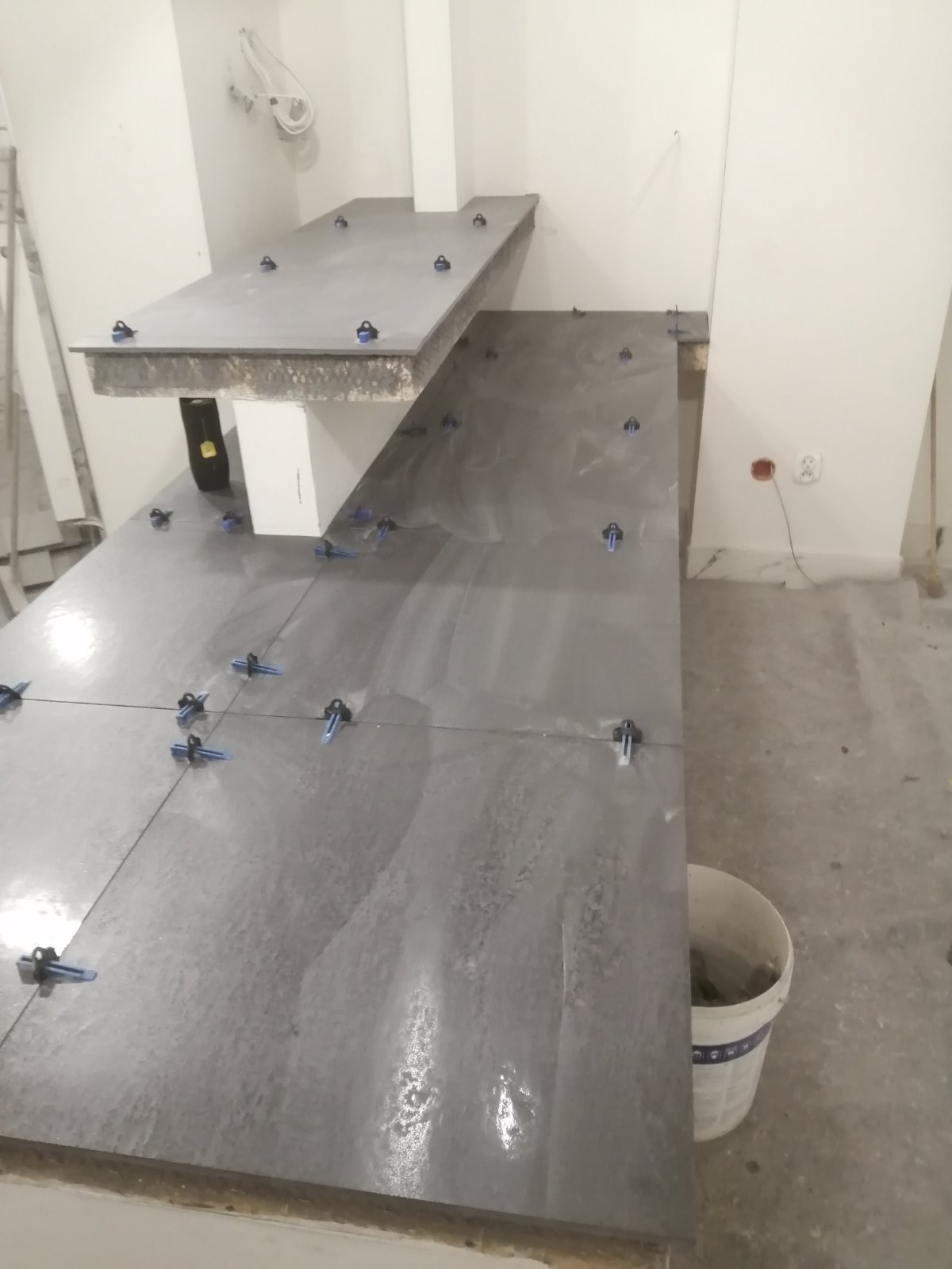 Układanie szarych płytek na blacie we Wrocławiu z użyciem klipsów poziomujących, widoczny kubeł z zaprawą.