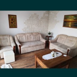 Tomasz www - Salon z beżowymi sofami, stolikiem kawowym z koronkową serwetą i dekoracyjną ścianą z kamienia, oświetlony ciepłym światłem.