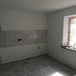 Tomasz www - Wnętrze kuchni w trakcie remontu, widoczne ułożone płytki nad blatem, niepodłączone kable elektryczne zwisające ze ściany oraz okno zabezpieczone folią malarską.
