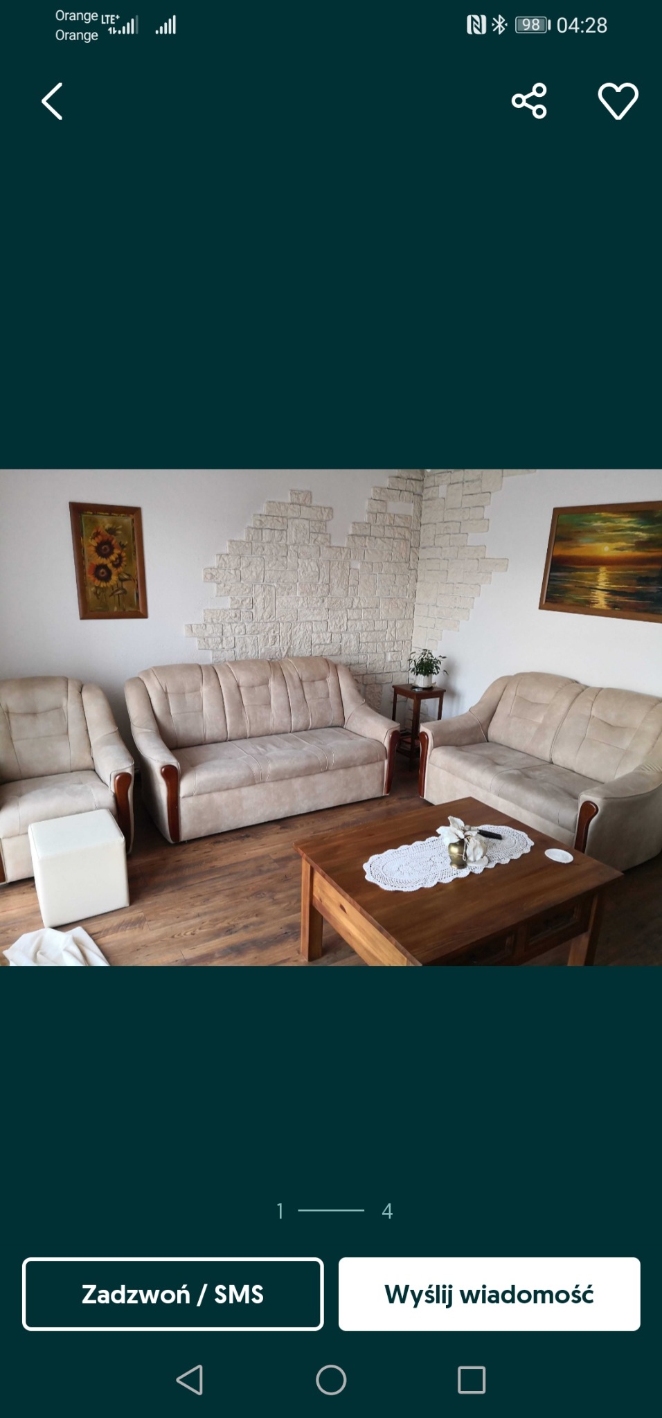 Salon z beżowymi sofami, stolikiem kawowym z koronkową serwetą i dekoracyjną ścianą z kamienia, oświetlony ciepłym światłem.