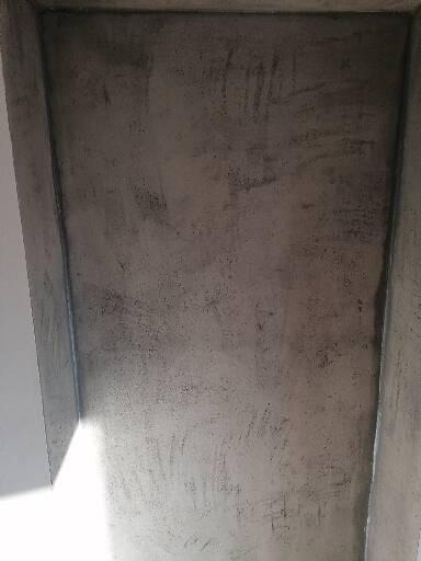 Surowa ściana narożna z widocznymi śladami po szpachlowaniu, przygotowana do dalszych prac wykończeniowych.