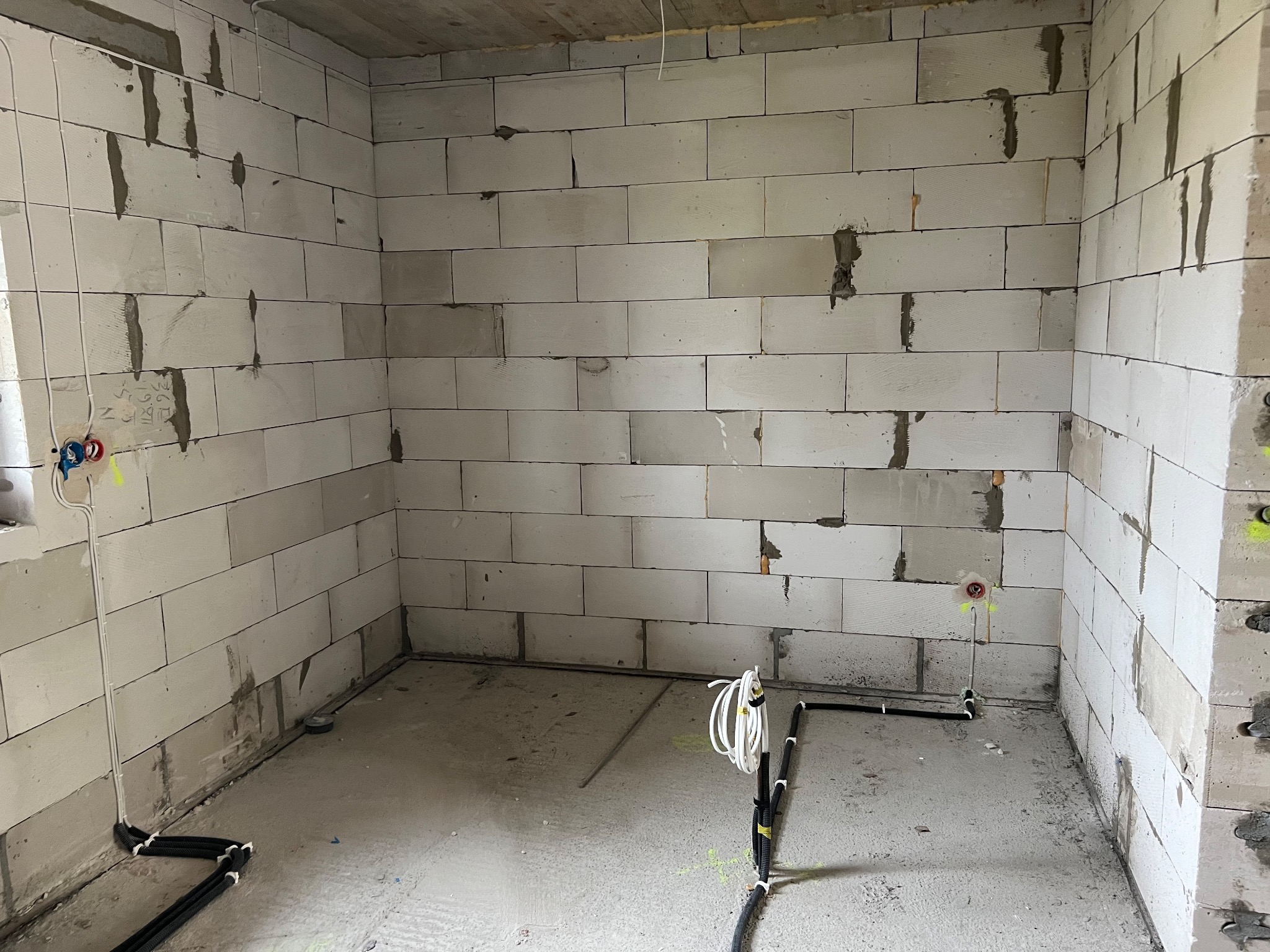 Surowy stan wnętrza z bloczków, widoczne przewody elektryczne w peszlach układane wzdłuż ścian i podłogi, przygotowane punkty pod gniazdka i włączniki.