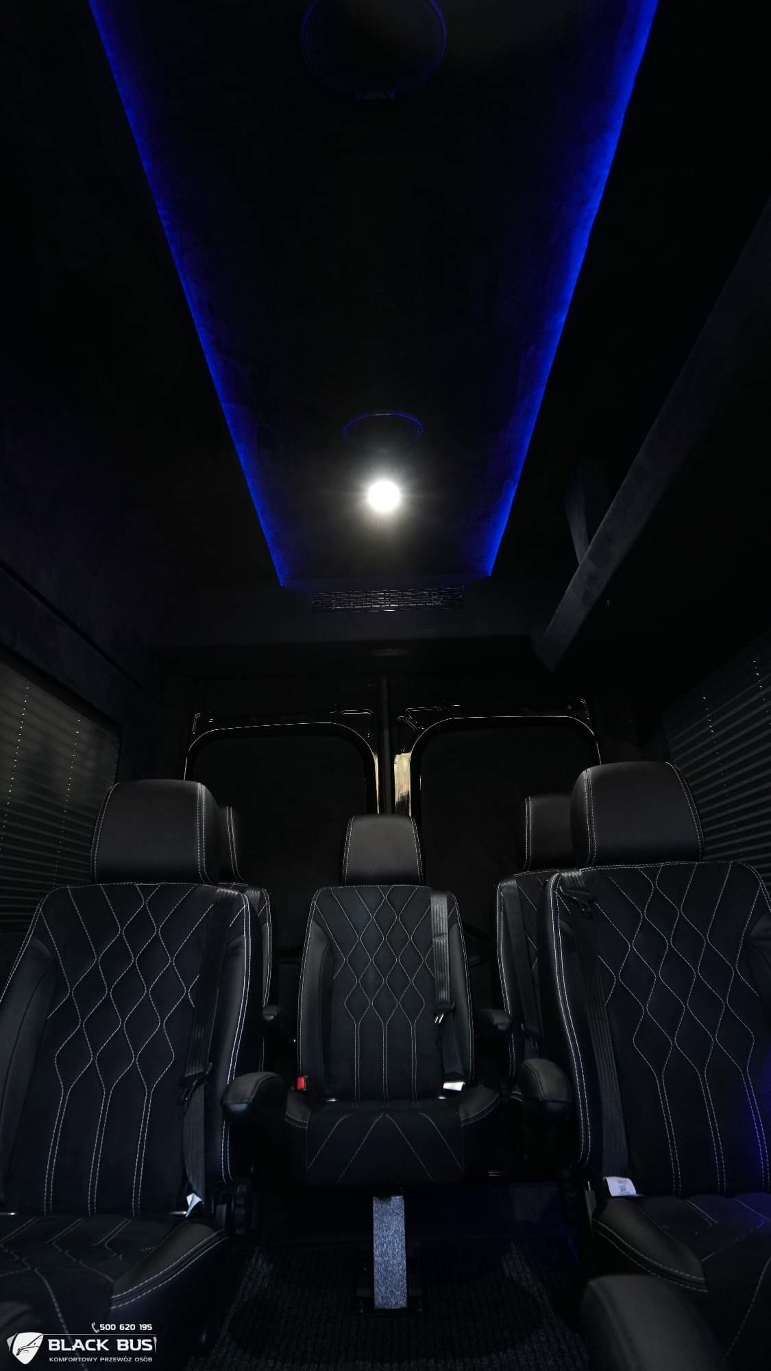 Wnętrze luksusowego busa z czarnymi skórzanymi fotelami z białymi przeszyciami w romby, oświetlenie sufitowe LED w kolorze niebieskim, widok z tyłu kabiny.