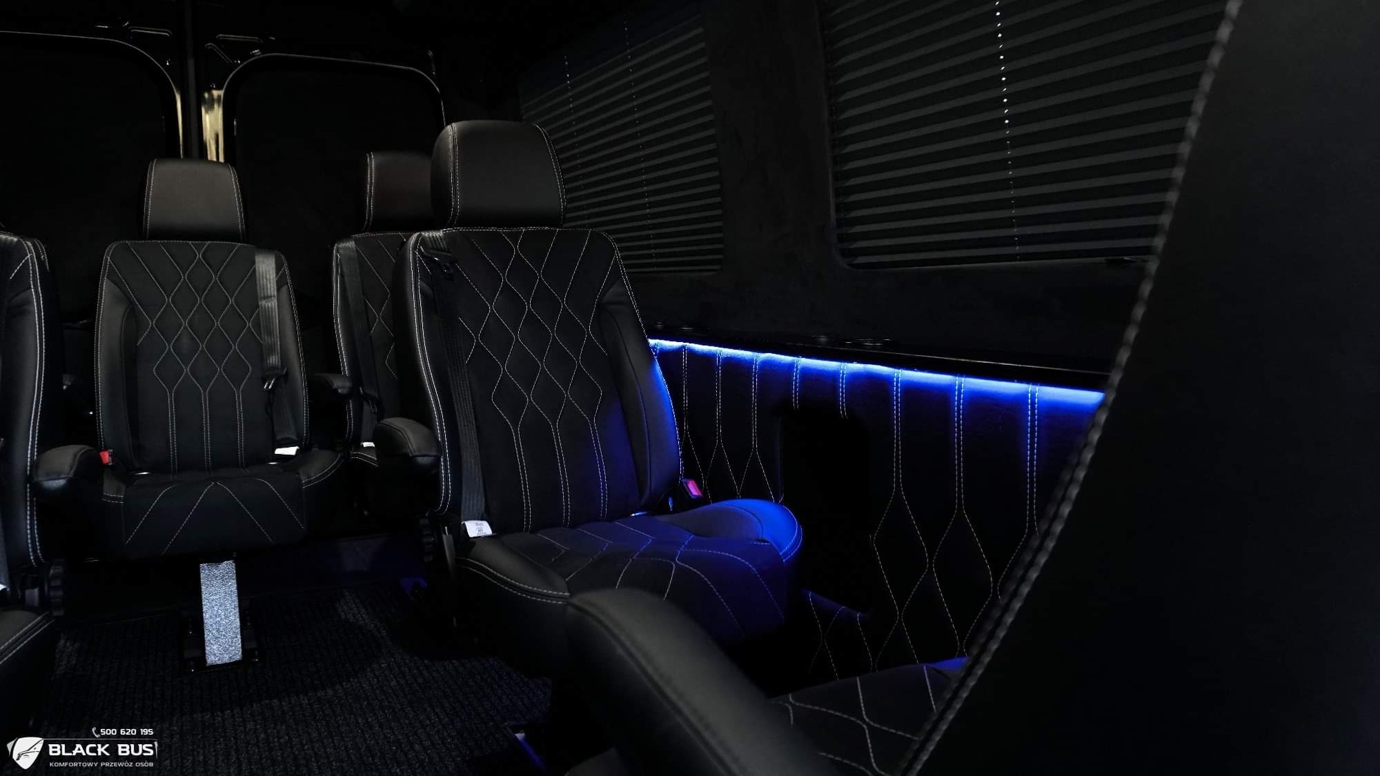 Wnętrze luksusowego busa z czarnymi skórzanymi fotelami przeszywanymi białym romboidalnym wzorem i nastrojowym niebieskim oświetleniem LED.