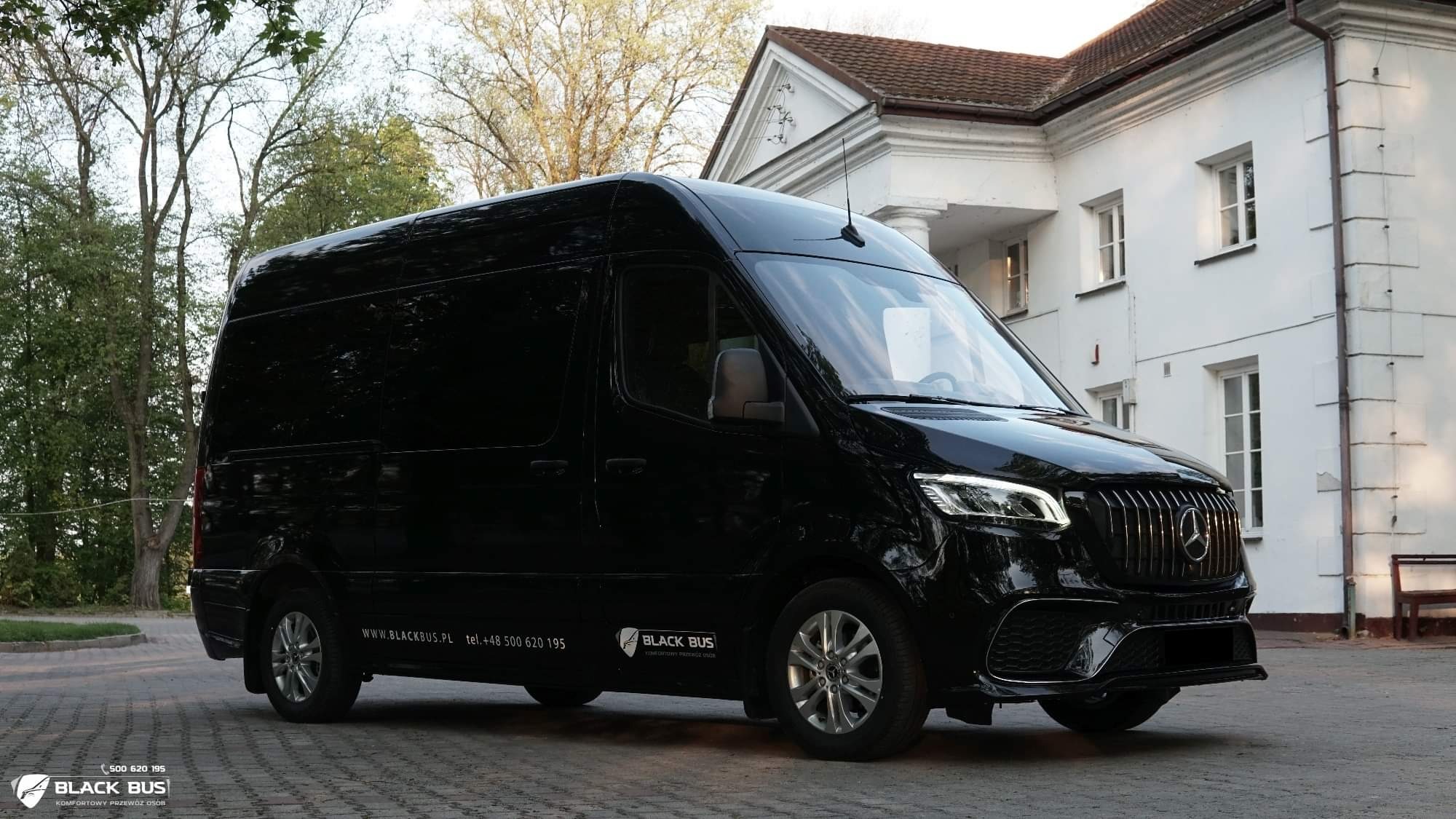 Czarny, luksusowy bus marki Mercedes z logo firmy 'Black Bus' zaparkowany przed białym, klasycznym budynkiem z kolumnami.