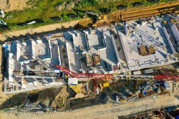 Widok z góry na plac budowy z fundamentami i ścianami budynku żelbetowego w trakcie wznoszenia, z widocznym żurawiem wieżowym i przygotowanym terenem.