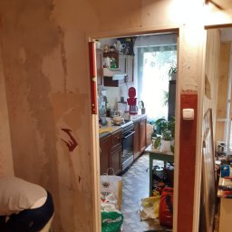 Emt Serwis Tomasz Sobutka - Demontaż starej tapety w pokoju przed remontem kuchni, widoczne ślady po tapecie na ścianie, poziomica na framudze drzwi, w tle wyposażenie kuchni.