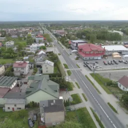 Panorama małego miasteczka z lotu ptaka, widoczna główna ulica, zabudowa mieszkalna i usługowa, kościół z czerwoną wieżą w oddali.