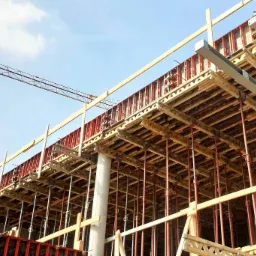 Budowa obiektu: widok z dołu na szalunki stropowe, podpory stalowe i żuraw budowlany na tle błękitnego nieba.