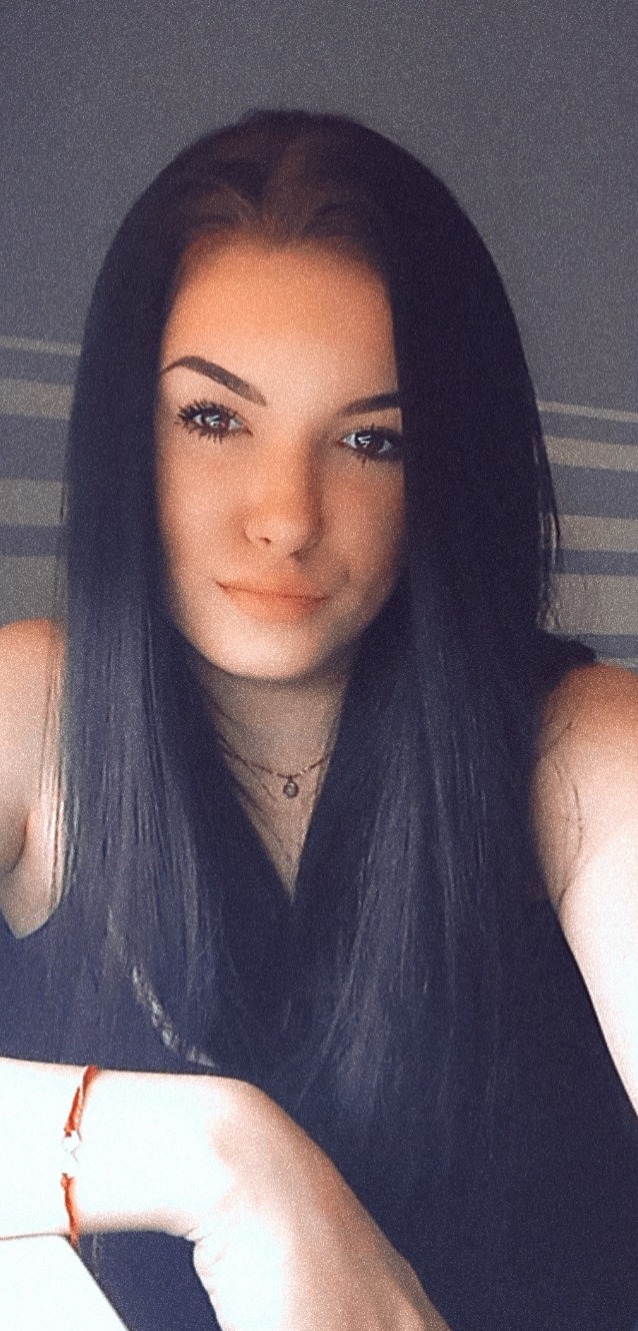 Portret młodej kobiety z długimi, czarnymi włosami, delikatnym makijażem i subtelną biżuterią na szyi.