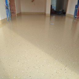 RAMI FLOOR RAFAŁ KLOCEK, MICHAŁ GORCZYCA SPÓŁKA CYWILNA - Beżowa, gładka posadzka z drobnymi, ciemnymi i jasnymi plamkami. Widoczne rury przy ścianie i wejście do innego pomieszczenia w tle.