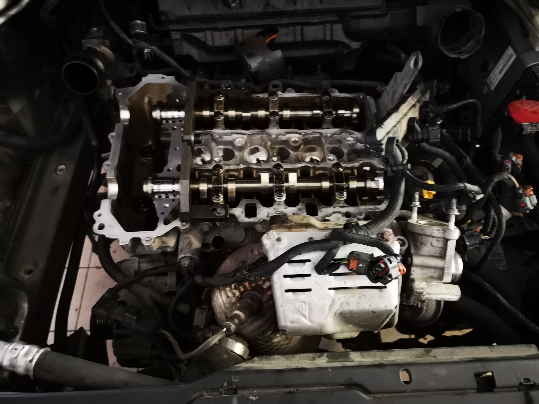 Widok z bliska na rozłożony silnik samochodowy z widocznymi wałkami rozrządu, przewodami i osprzętem, w trakcie naprawy lub diagnostyki.