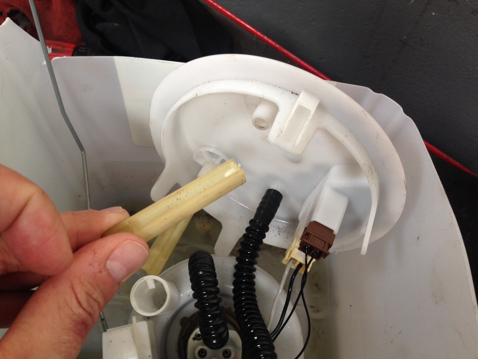 Demontaż pompy paliwa w samochodzie w Piotrków Trybunalski: widoczny element z tworzywa sztucznego w dłoni, czarne przewody i biała obudowa.