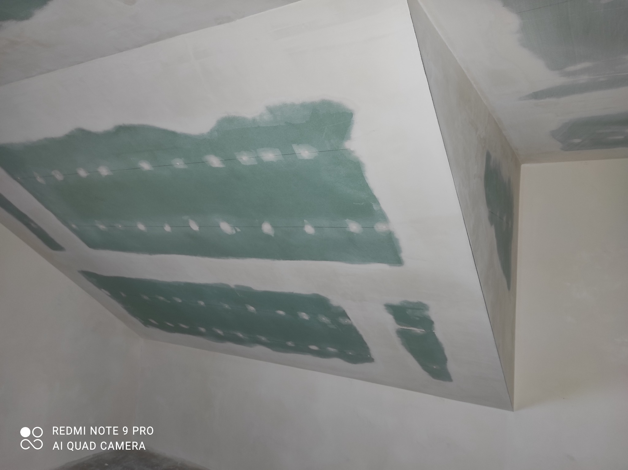 Sufit podwieszany z płyt gipsowo-kartonowych, częściowo zaszpachlowany, widoczne miejsca łączeń płyt i ślady po wkrętach.