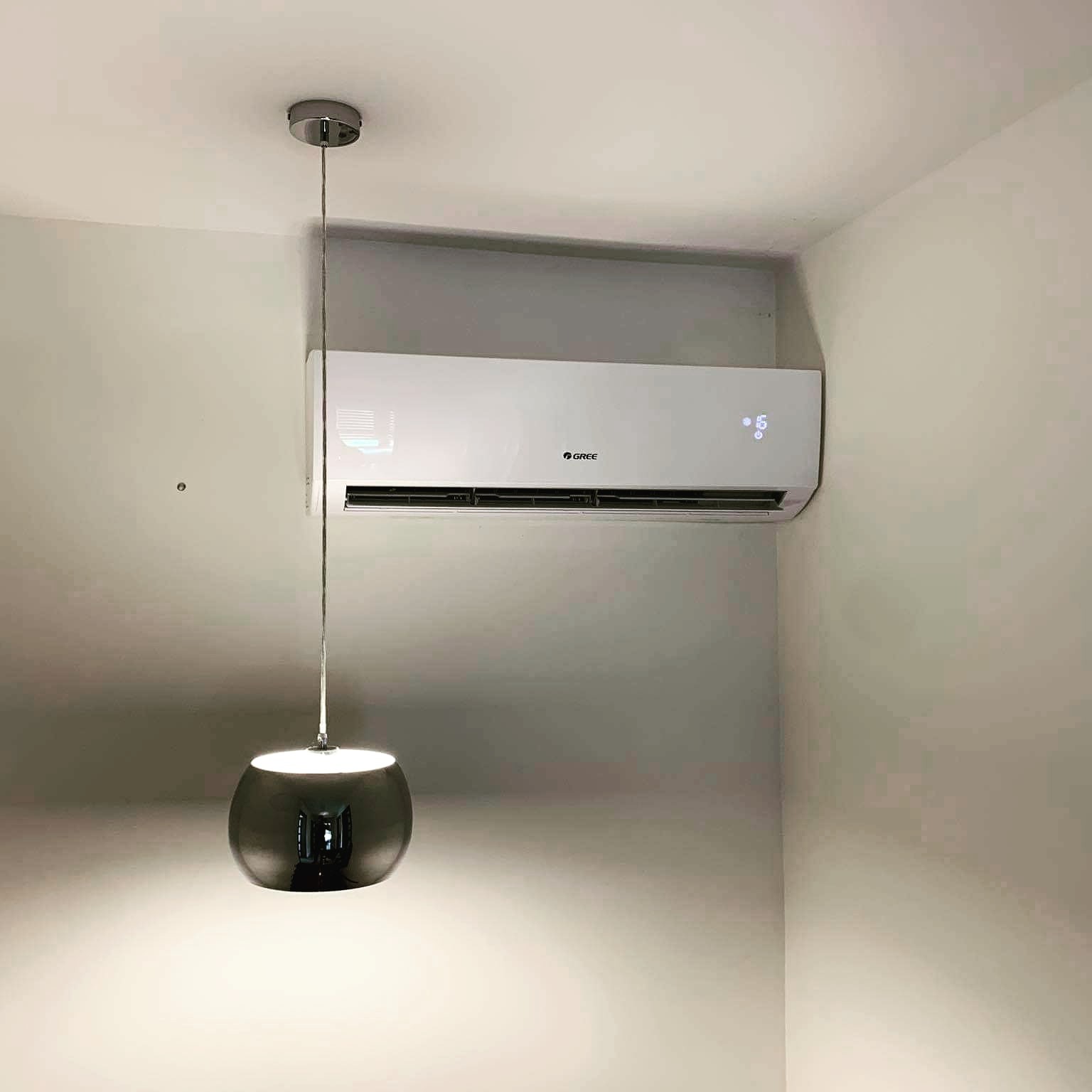 Zamontowana jednostka wewnętrzna marki Gree na ścianie w pomieszczeniu, widoczna także nowoczesna lampa wisząca z metalowym kloszem.