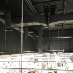 Widok z góry na system kanałów wentylacyjnych w hali sklepu, z widocznymi elementami instalacji nad regałami z towarem.
