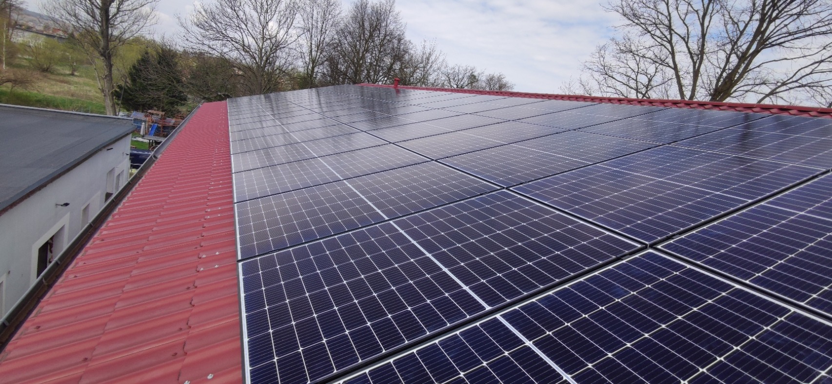 Panele słoneczne na czerwonym dachu w Rudzie Śląskiej, widok z góry, w tle drzewa bez liści.