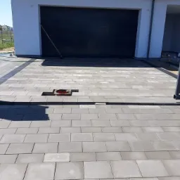 Ułożona szara kostka brukowa przed garażem w Gdańsku, widoczny fragment studzienki kanalizacyjnej i brama wjazdowa.