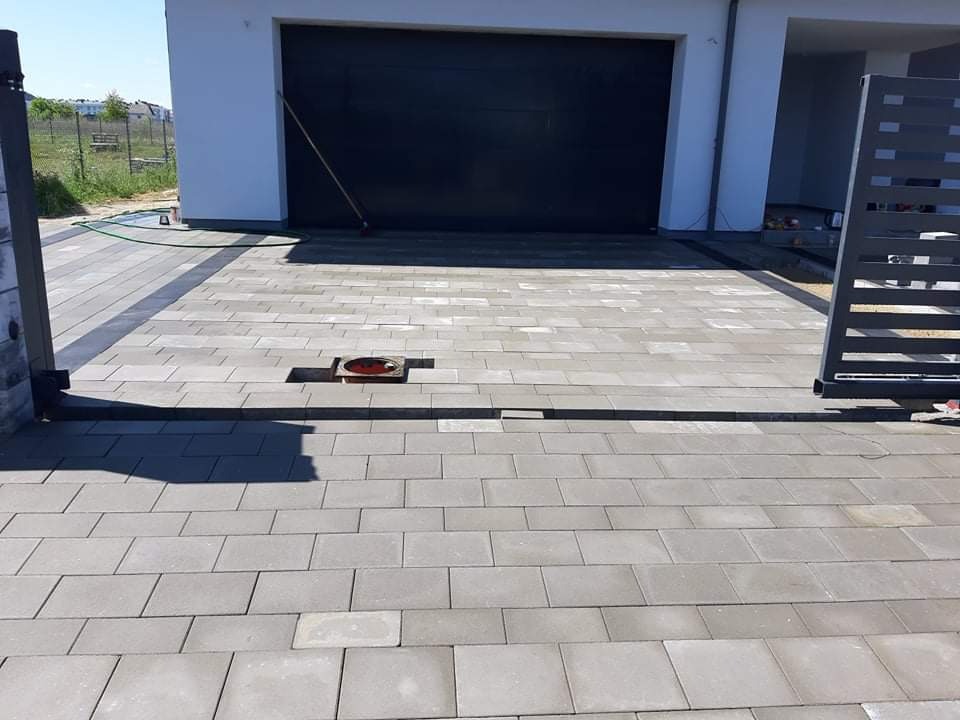 Ułożona szara kostka brukowa przed garażem w Gdańsku, widoczny fragment studzienki kanalizacyjnej i brama wjazdowa.