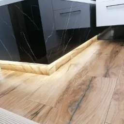 Ułożona podłoga z paneli imitujących drewno w łazience, z podświetleniem LED u dołu zabudowy szafek z czarnym marmurkowym wykończeniem.