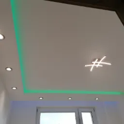 Biały podwieszany sufit z oświetleniem LED w kolorze zielonym i punktowymi lampami, dodatkowo nowoczesna lampa sufitowa w kształcie krzyża