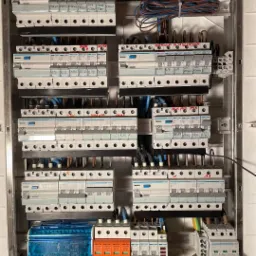 Rozdzielnica elektryczna z zainstalowanymi zabezpieczeniami przepięciowymi PRO-TEC, bezpiecznikami Hager i okablowaniem, widoczne oznaczenia obwodów i komponentów.