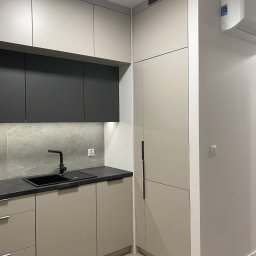 Masalon Design - Nowoczesna kuchnia w odcieniach beżu i szarości z czarną armaturą i blatem. Minimalistyczny design, gładkie fronty szafek, oświetlenie LED pod szafkami górnymi.