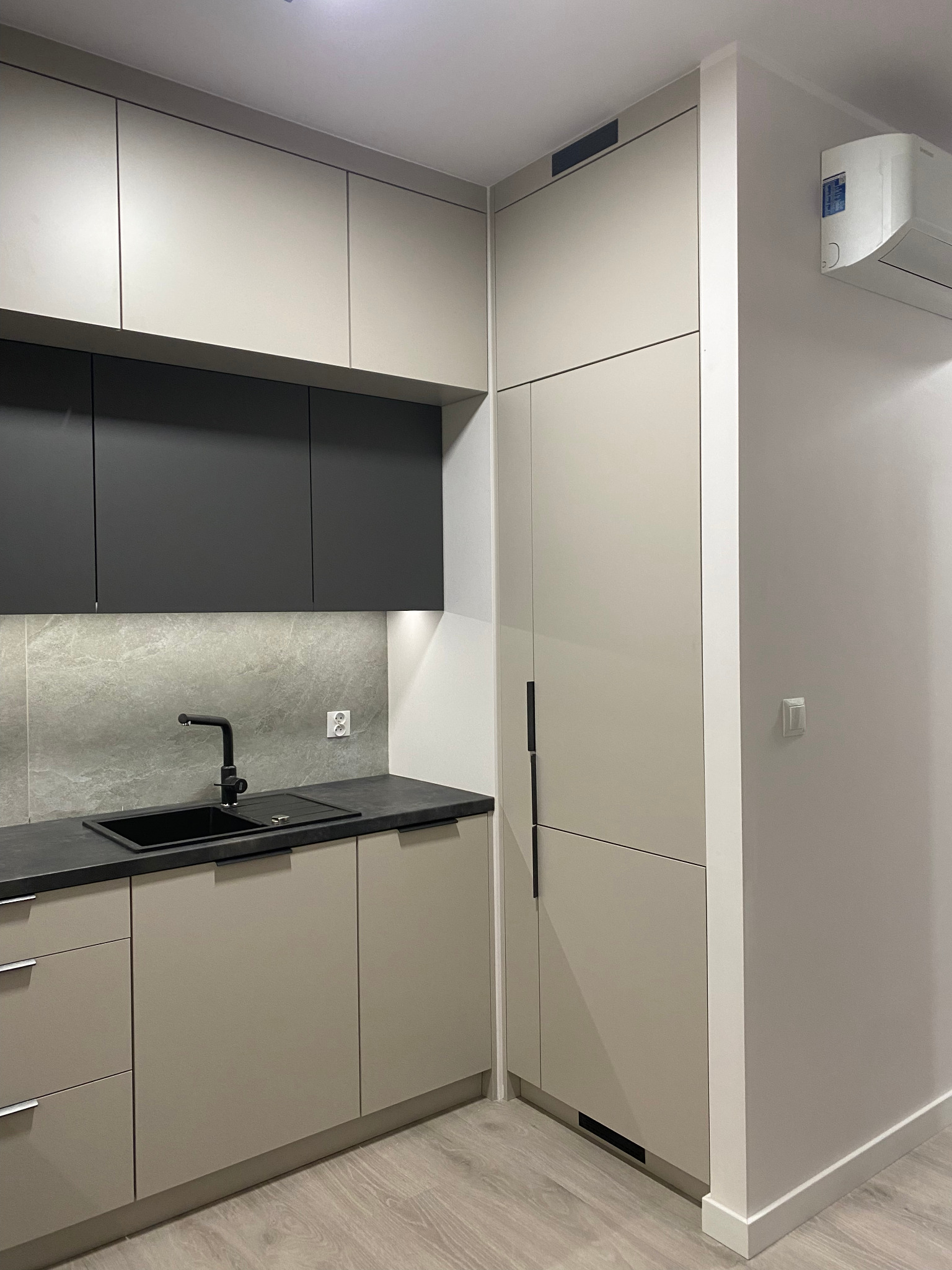 Nowoczesna kuchnia w odcieniach beżu i szarości z czarną armaturą i blatem. Minimalistyczny design, gładkie fronty szafek, oświetlenie LED pod szafkami górnymi.