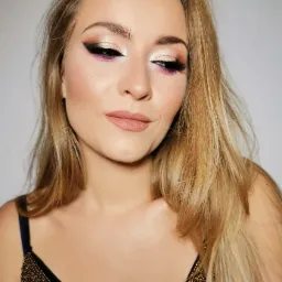 Portret kobiety z profesjonalnie wykonanym, wieczorowym wizażem, obejmującym złote cienie, czarny eyeliner i akcenty różu, w czarnej sukience z ozdobnymi, złotymi koralikami.