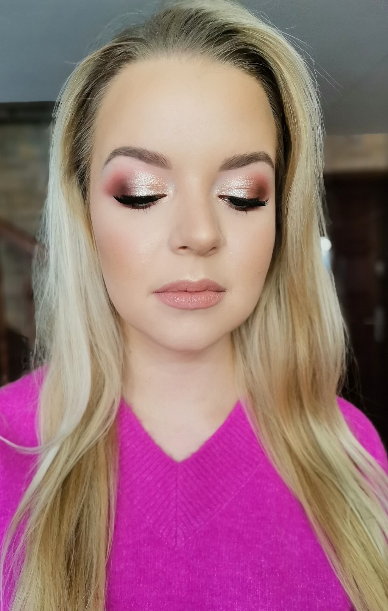 Portret kobiety z zamkniętymi oczami prezentującej delikatny, błyszczący cień do powiek w odcieniach różu i złota z czarną kreską, oraz jasnoróżową pomadkę na ustach, w różowym swetrze.