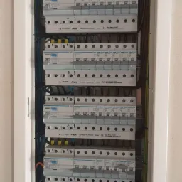 Rozdzielnica elektryczna z zabezpieczeniami Hager, widoczne bezpieczniki, ograniczniki przepięć i listwy zaciskowe, przewody ułożone wewnątrz obudowy.