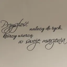 Czarny, ozdobny napis na kremowej ścianie: Przyszłość należy do tych, którzy wierzą w swoje marzenia.