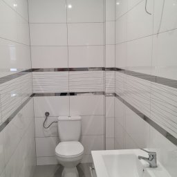 BRH Bracia Hudony usługi budowlane i wykończeniowe Maciej Hudon - Nowoczesna łazienka z białymi płytkami, ozdobnym pasem z szarymi liniami, umywalką na szafce z chromowaną armaturą i toaletą.