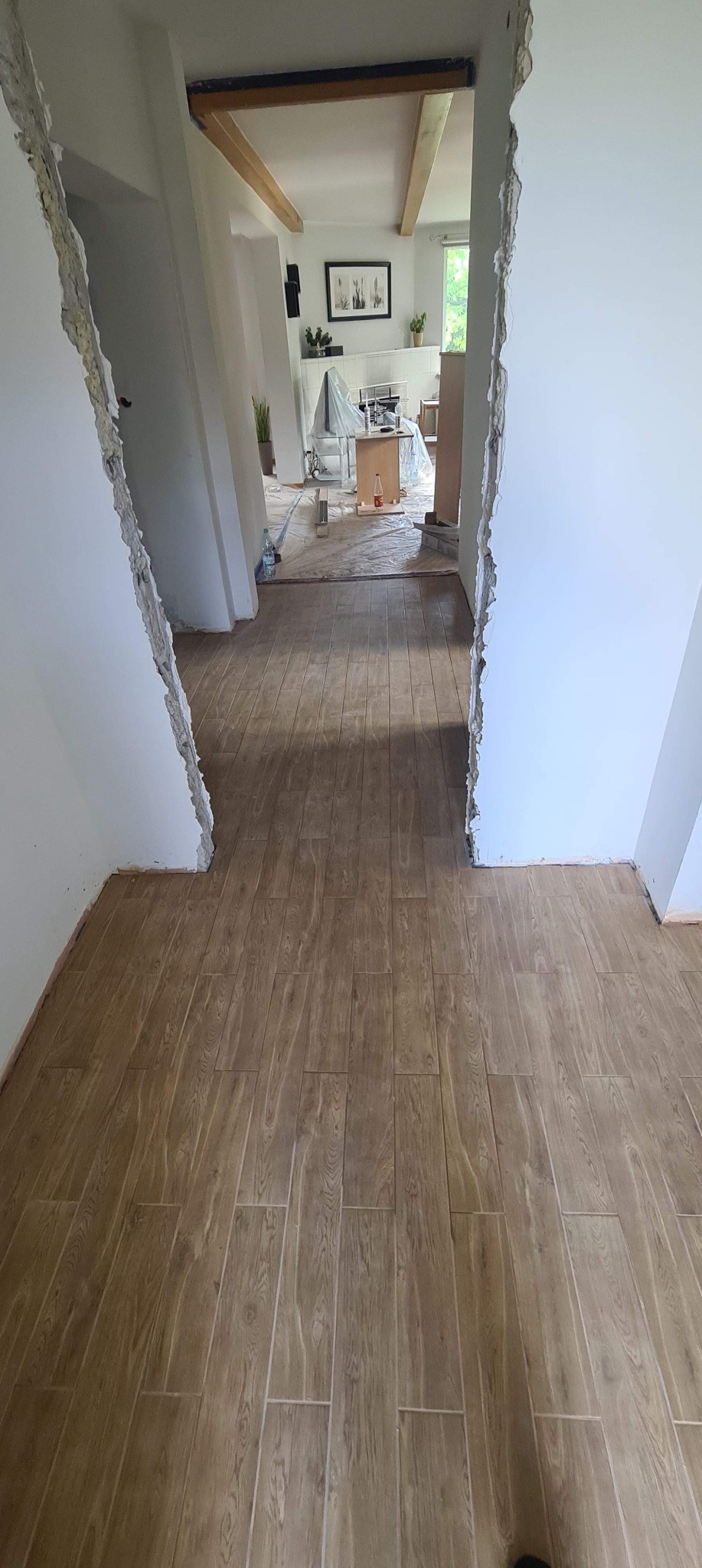 Ułożona podłoga z płytek imitujących drewno w trakcie prac wykończeniowych, widoczne surowe krawędzie ścian i przygotowane pomieszczenie w tle.