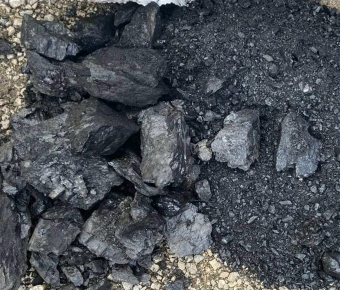 Góra brył węgla kamiennego, częściowo rozdrobnionego, ułożona na ziemi z widocznymi drobnymi kamykami.