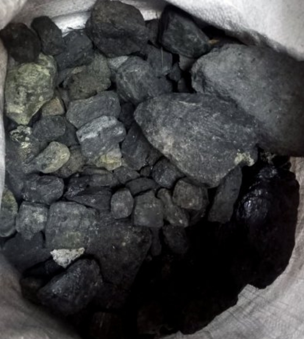 Worek wypełniony bryłami węgla o nieregularnych kształtach i zróżnicowanej kolorystyce, od grafitowej po antracytową, z widocznymi refleksami światła na niektórych powierzchniach.