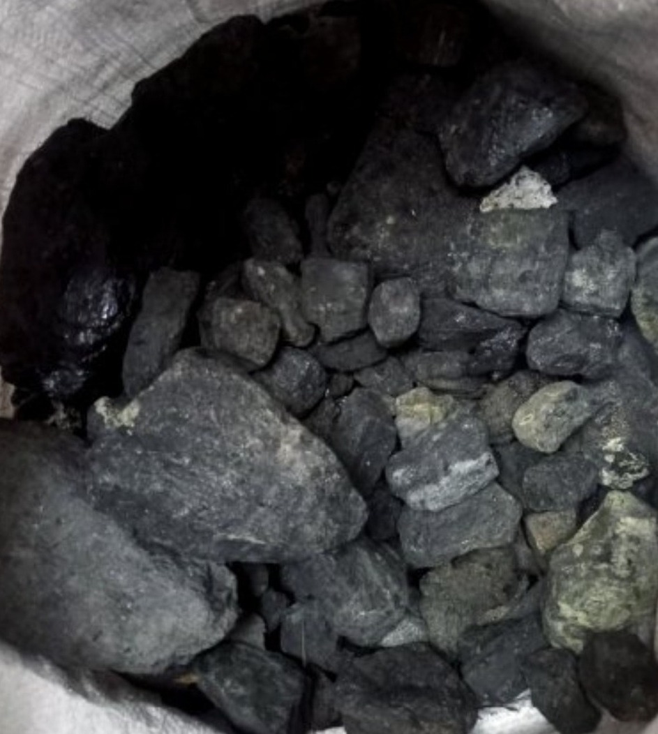 Worek wypełniony bryłami węgla o zróżnicowanej wielkości i fakturze, z widocznymi refleksami światła na niektórych powierzchniach.
