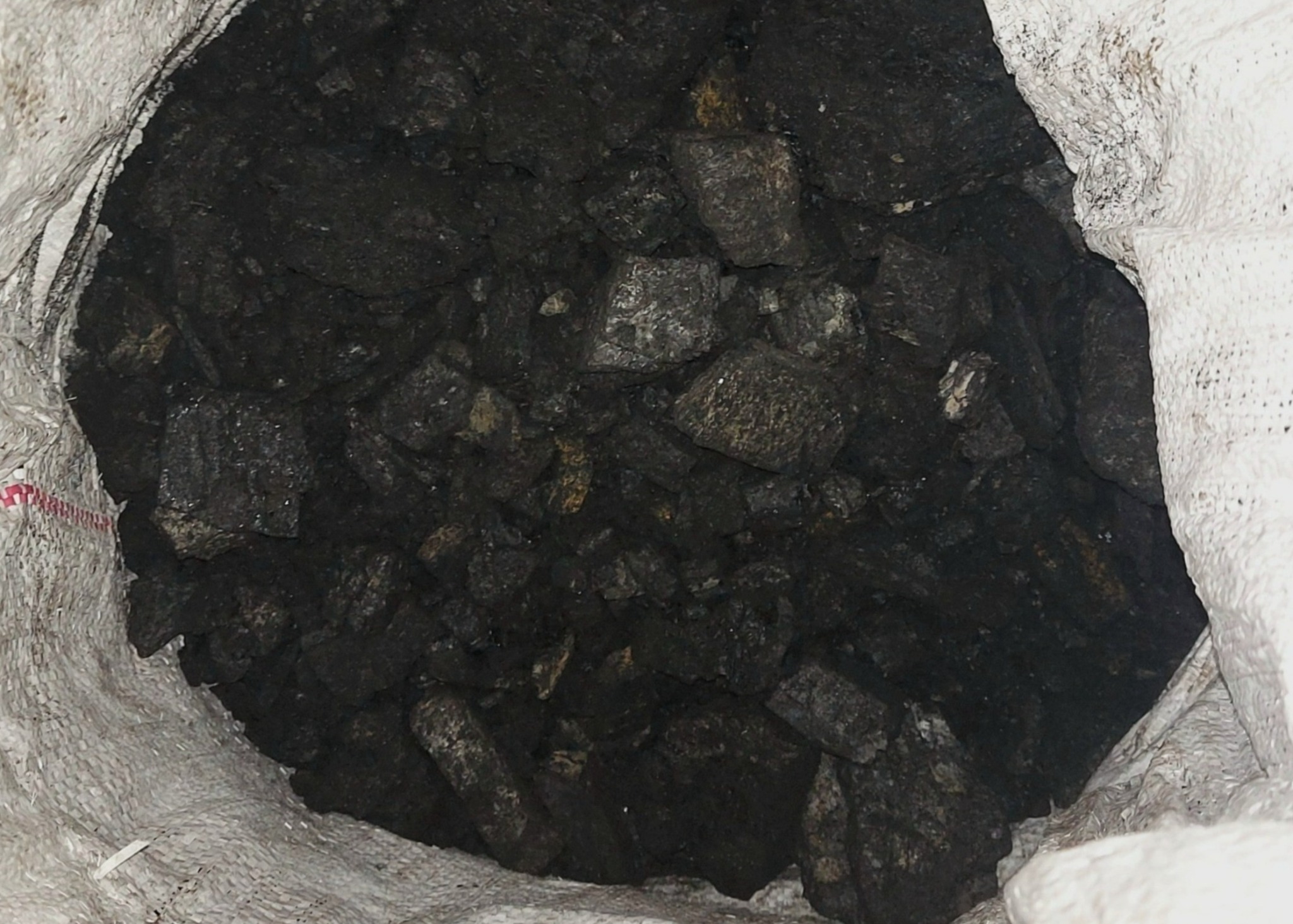Wnętrze worka wypełnionego bryłami ciemnego, błyszczącego węgla kamiennego, widoczne fragmenty białego, teksturowanego worka.