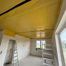 Dariusz Litwin Usługi remontowo-budowlane - Przygotowanie do montażu płyty karton gips: żółta folia paroizolacyjna z czarnymi paskami na suficie, aluminiowa drabina i rusztowanie w pustym, surowym pomieszczeniu z oknem.
