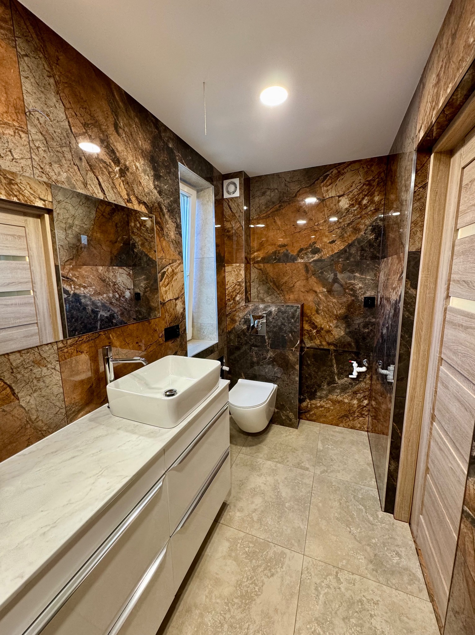 Wykończona łazienka w Zamościu z marmurowymi płytkami na ścianach. Nowoczesna umywalka nablatowa i toaleta podwieszana. Lustro nad umywalką.