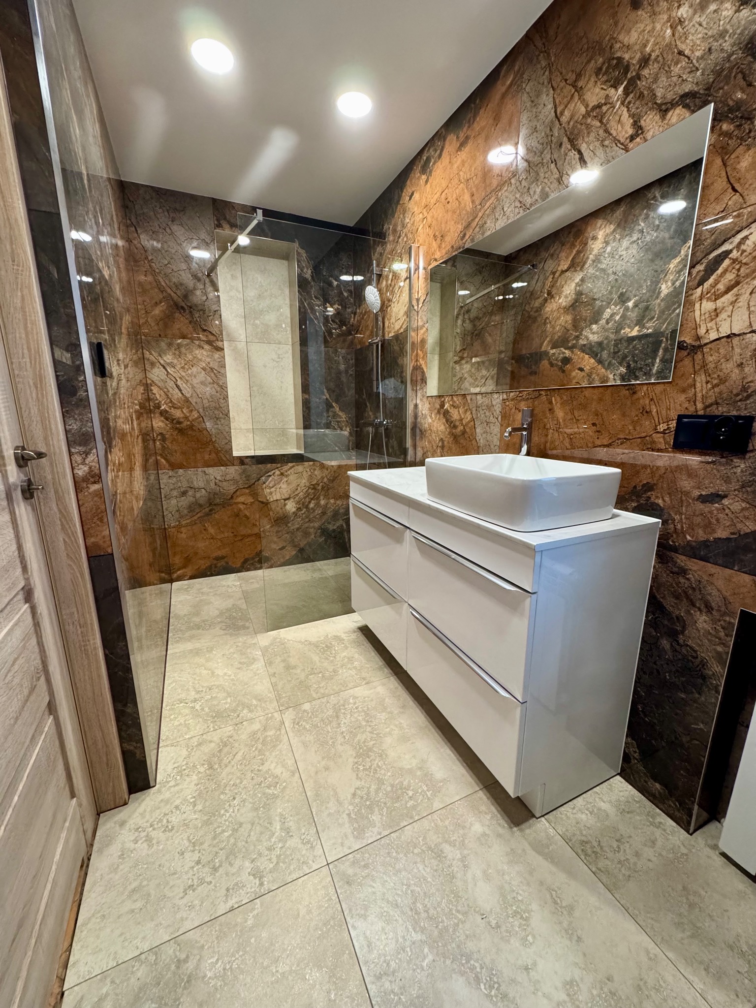 Nowoczesna łazienka z kabiną prysznicową typu walk-in, umywalką nablatową na białej szafce i płytkami imitującymi kamień. Widoczne detale wykończenia.