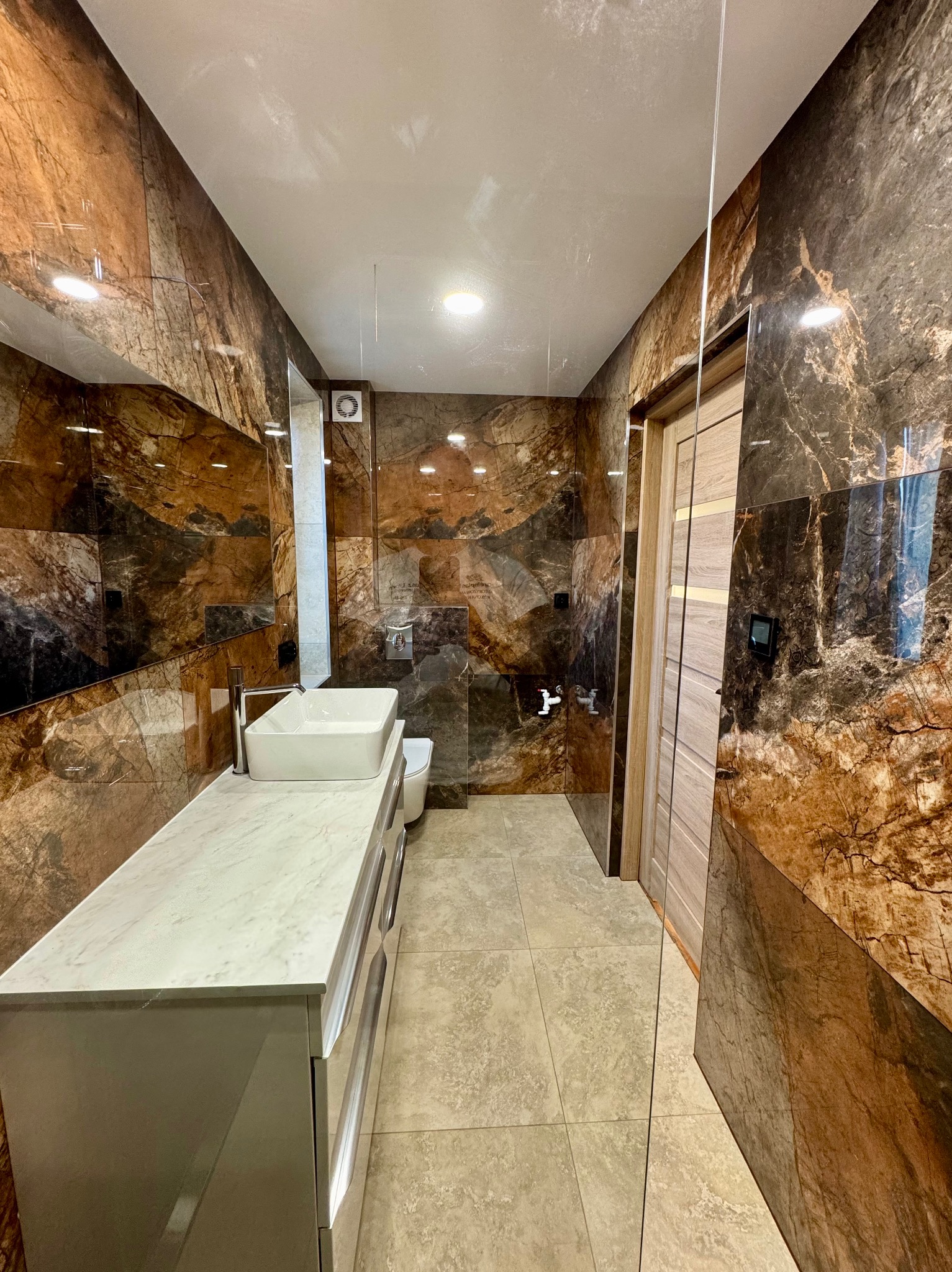 Nowoczesna łazienka z marmurowymi płytkami na ścianach, białą umywalką nablatową i przesuwnymi drzwiami z jasnego drewna.