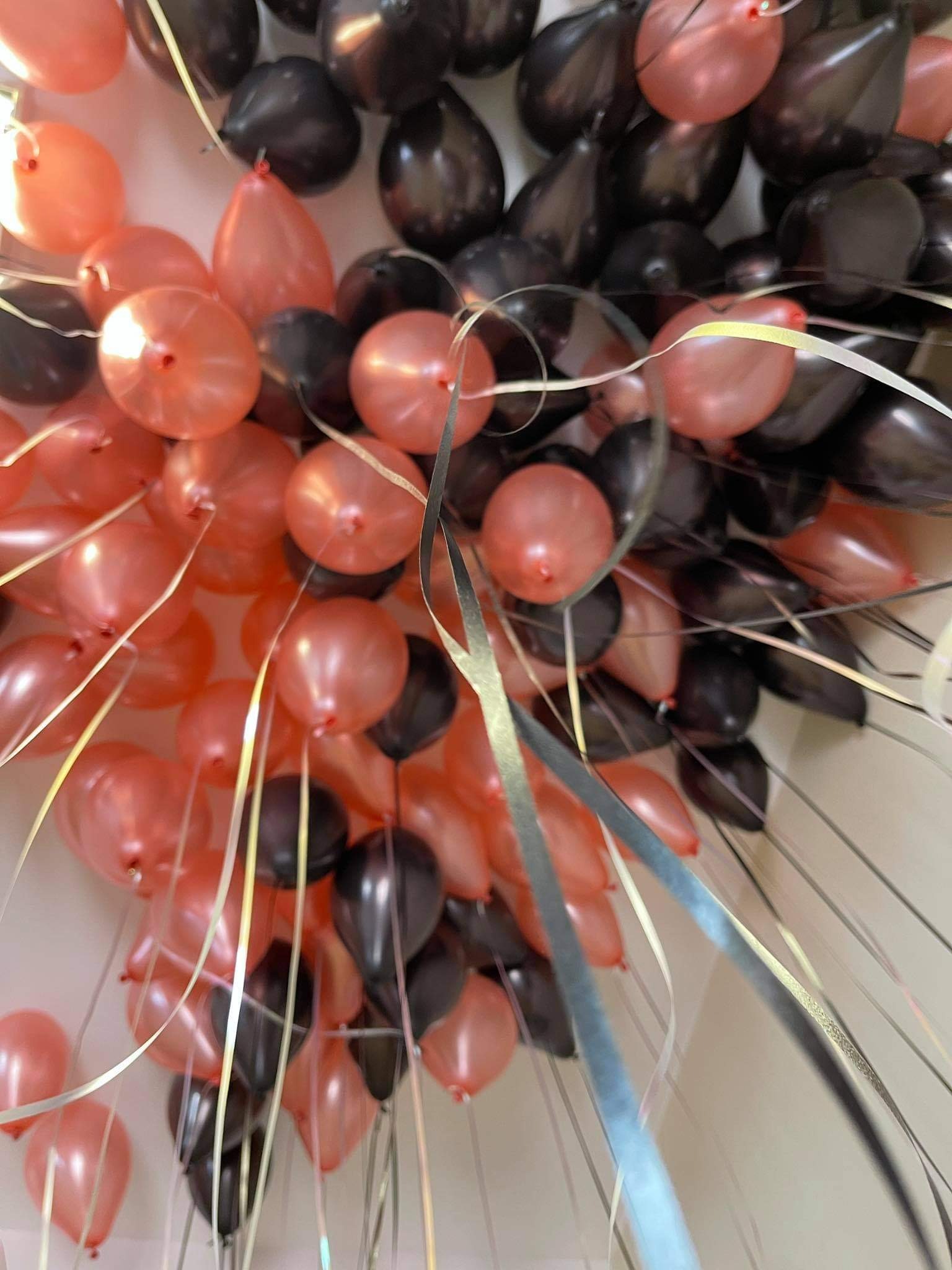 Dekoracja sufitu z czarnych i łososiowych balonów z błyszczącymi srebrnymi wstążkami, widok z dołu.