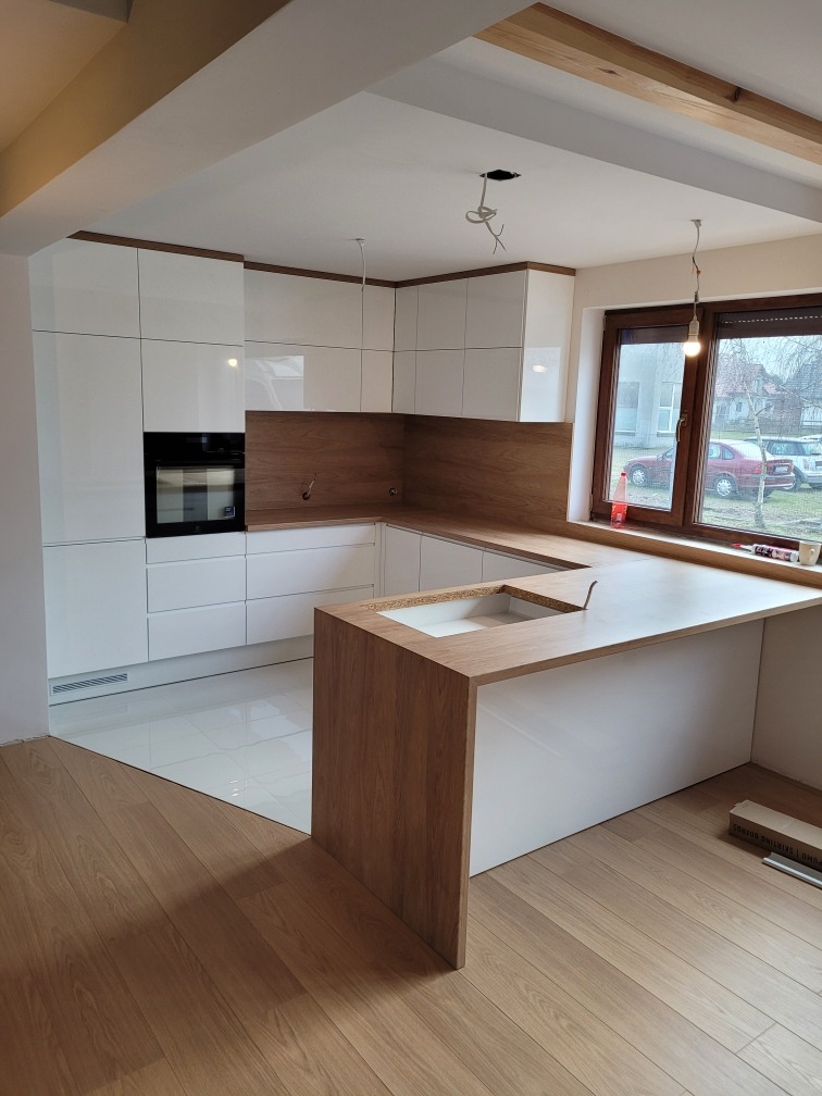Nowoczesna kuchnia z białymi szafkami i drewnianym blatem, widoczne niedokończone wykończenia sufitu i podłogi, okno z widokiem na zewnątrz.