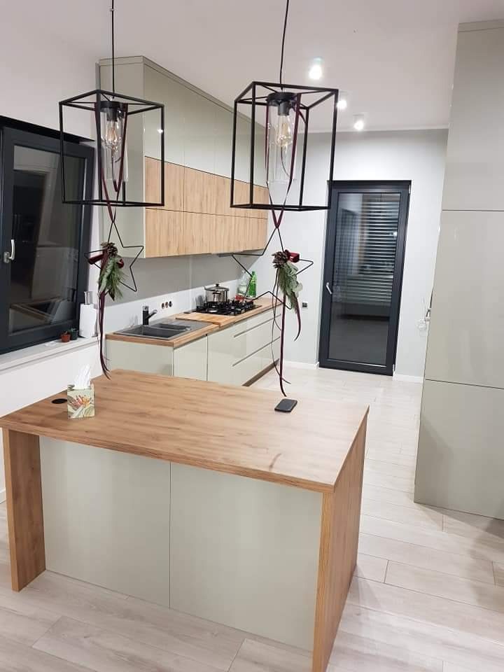 Nowoczesna kuchnia z wyspą, drewnianym blatem i szafkami w odcieniach beżu i bieli, oświetlona lampami w kształcie czarnych klatek, ozdobiona świątecznymi dekoracjami.