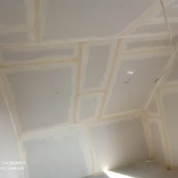 Poddasze z zamontowaną płytą kartonowo-gipsową, widoczne łączenia płyt wypełnione masą szpachlową przed szlifowaniem, z wiszącym kablem elektrycznym.