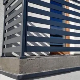 Nowoczesna brama wjazdowa w Maniewie z poziomymi, szarymi przęsłami i widocznym fragmentem okna w tle.