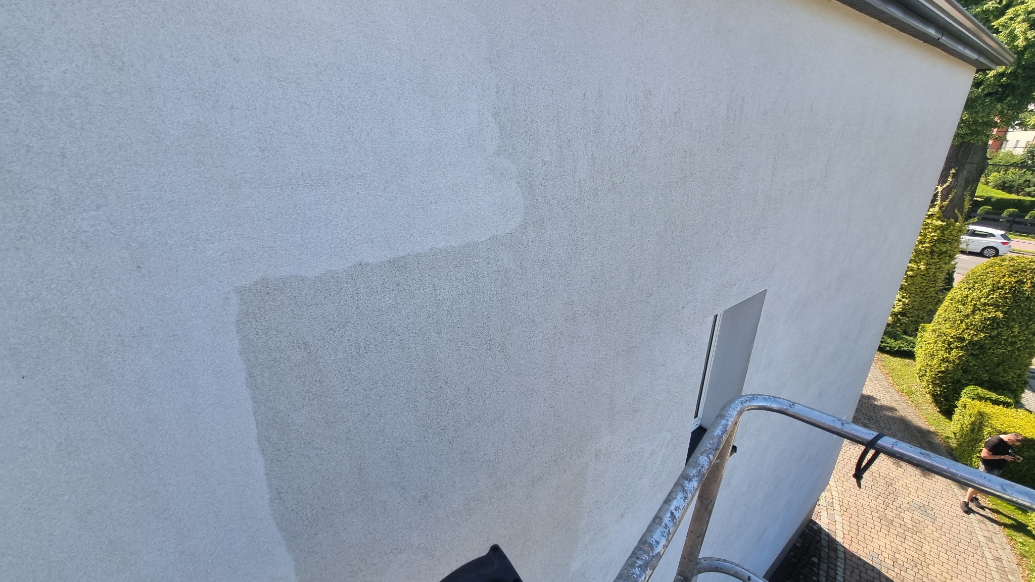 Ściana budynku z fragmentem umytej elewacji, ukazująca różnicę w kolorze i czystości powierzchni. Widoczny fragment rusztowania i otoczenie budynku.