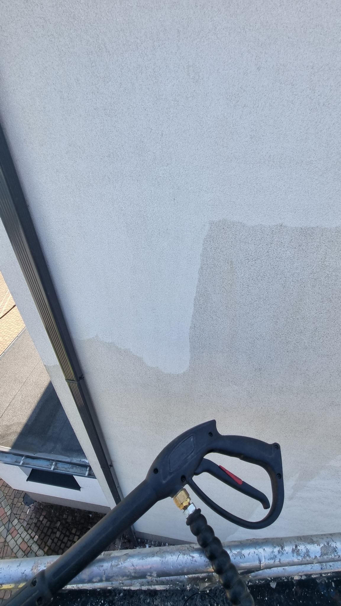 Elewacja budynku w trakcie czyszczenia myjką ciśnieniową, widoczna różnica w kolorze między umytą a brudną powierzchnią. Z bliska dysza myjki.