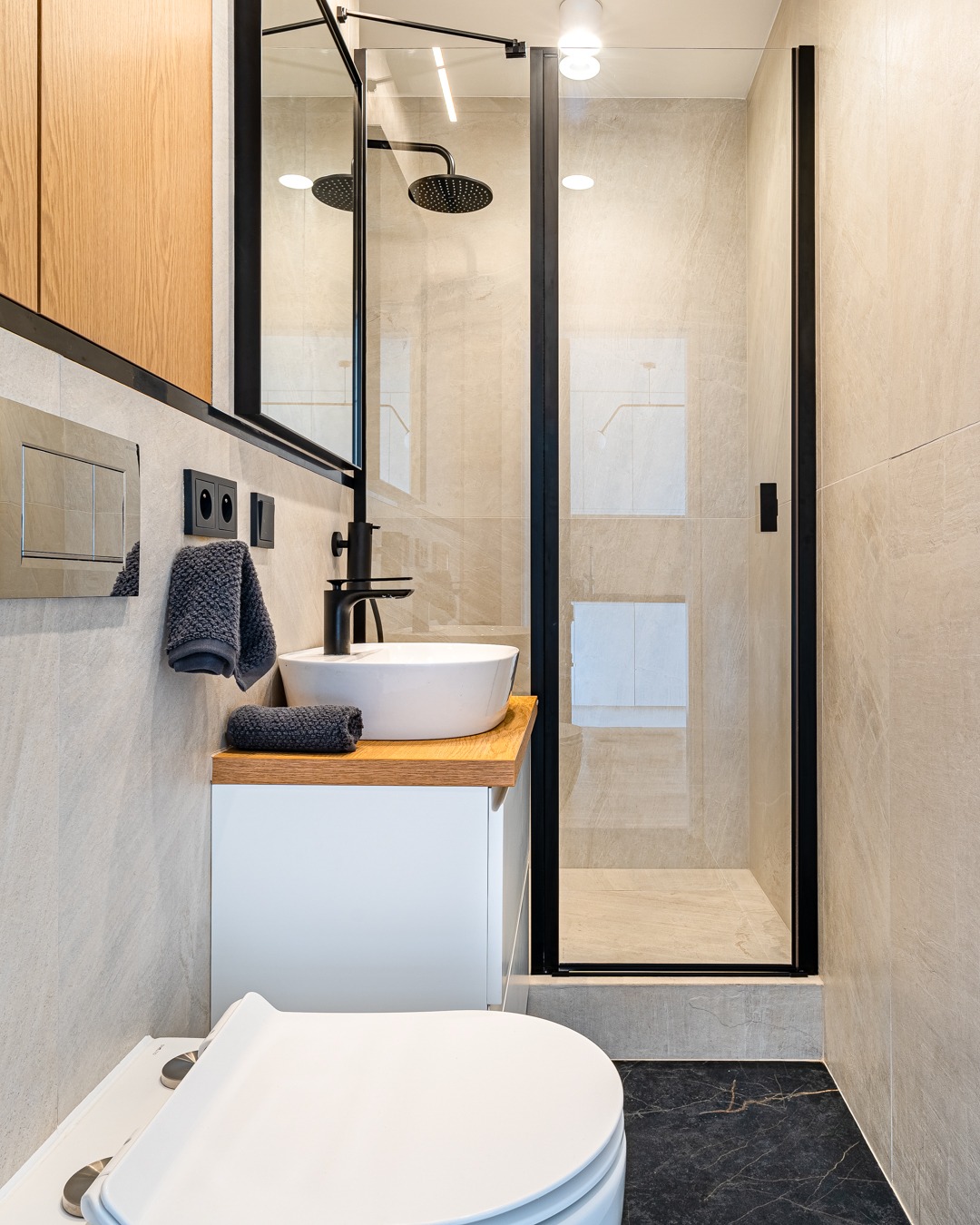 Nowoczesna łazienka z kabiną prysznicową typu walk-in, umywalką nablatową na drewnianym blacie, czarną armaturą i płytkami imitującymi marmur.
